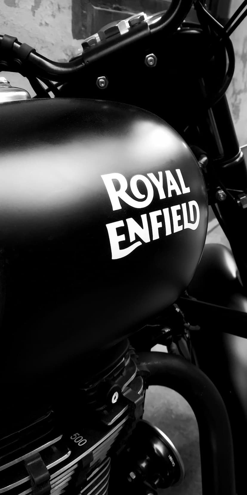 Royal Enfield motorcycle fuel tank in matte black features white logo lettering and mechanical engine details.