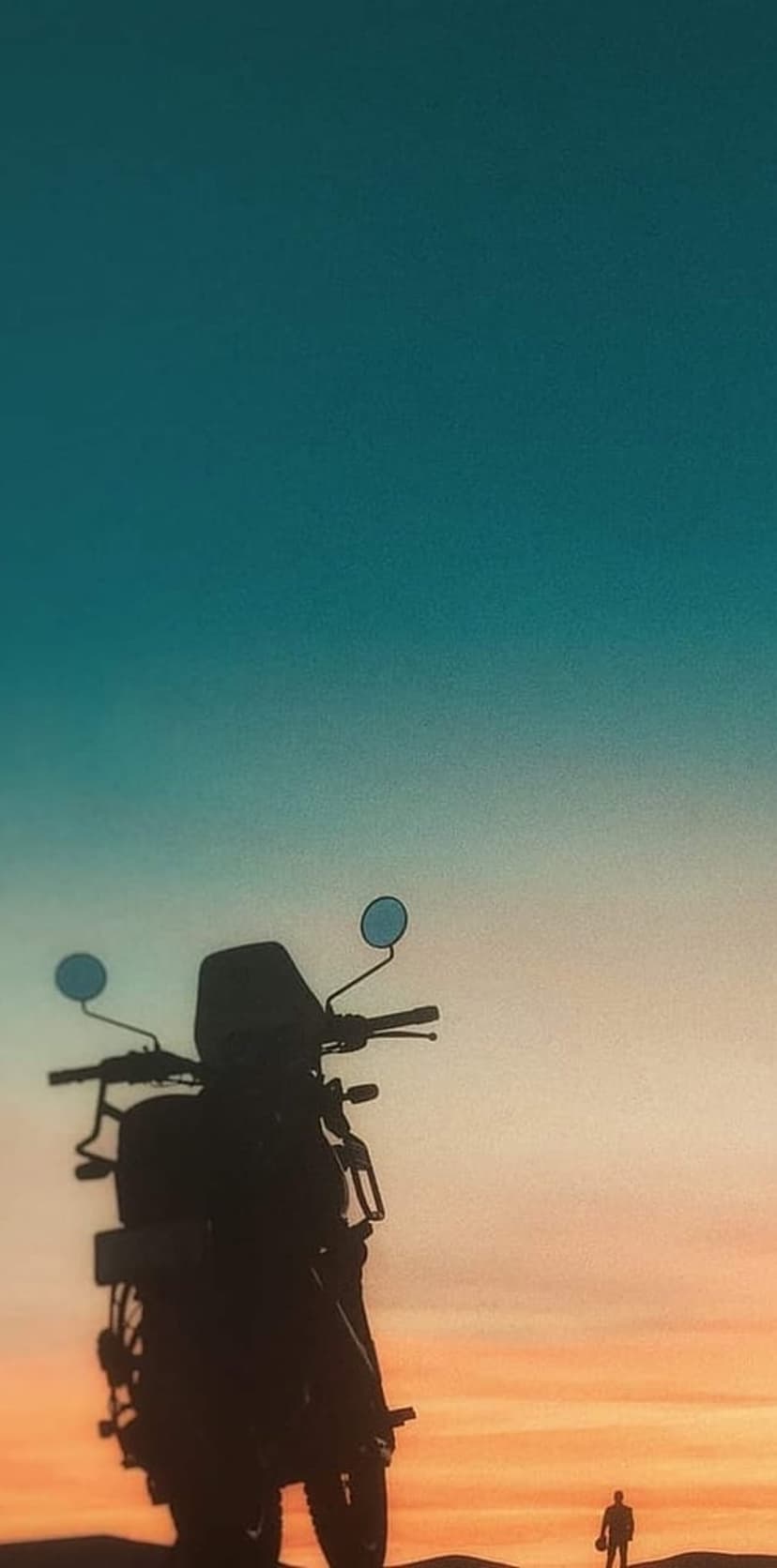 Silhouette of a person standing by a motorcycle during a vibrant desert sunset with a blue sky background.