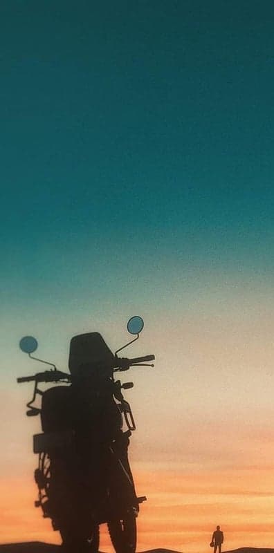 Silhouette of a motorcycle and person against sunset sky