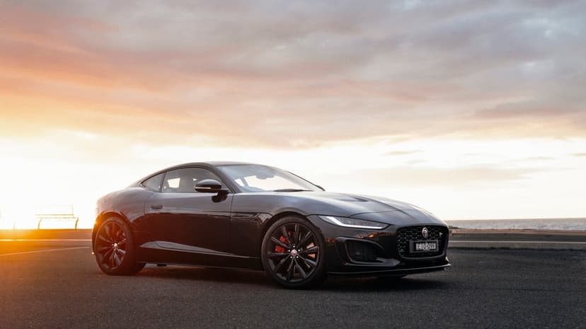 Black Jaguar sports car parked on a coastal road at sunset with orange light reflecting on the bodywork.