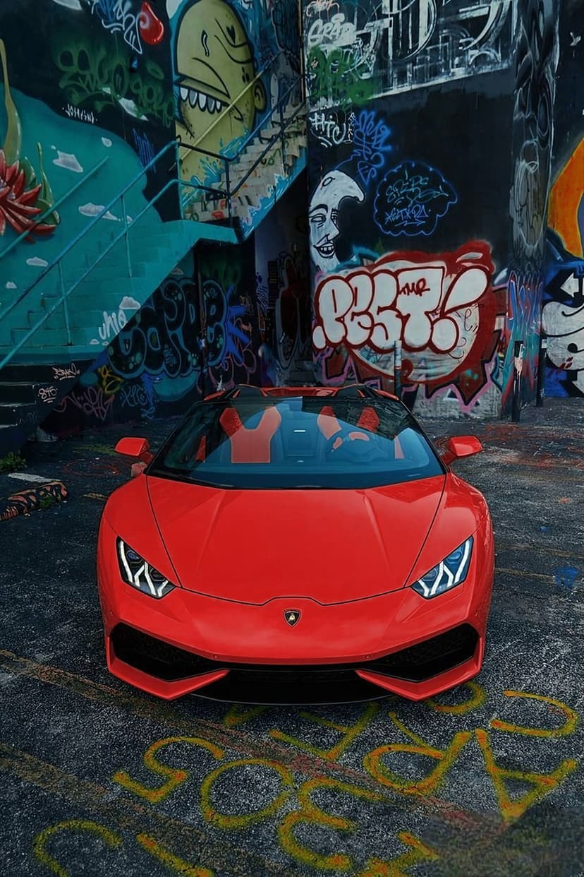 Red Lamborghini convertible parked on asphalt in front of a colorful, complex graffiti mural in an urban setting.