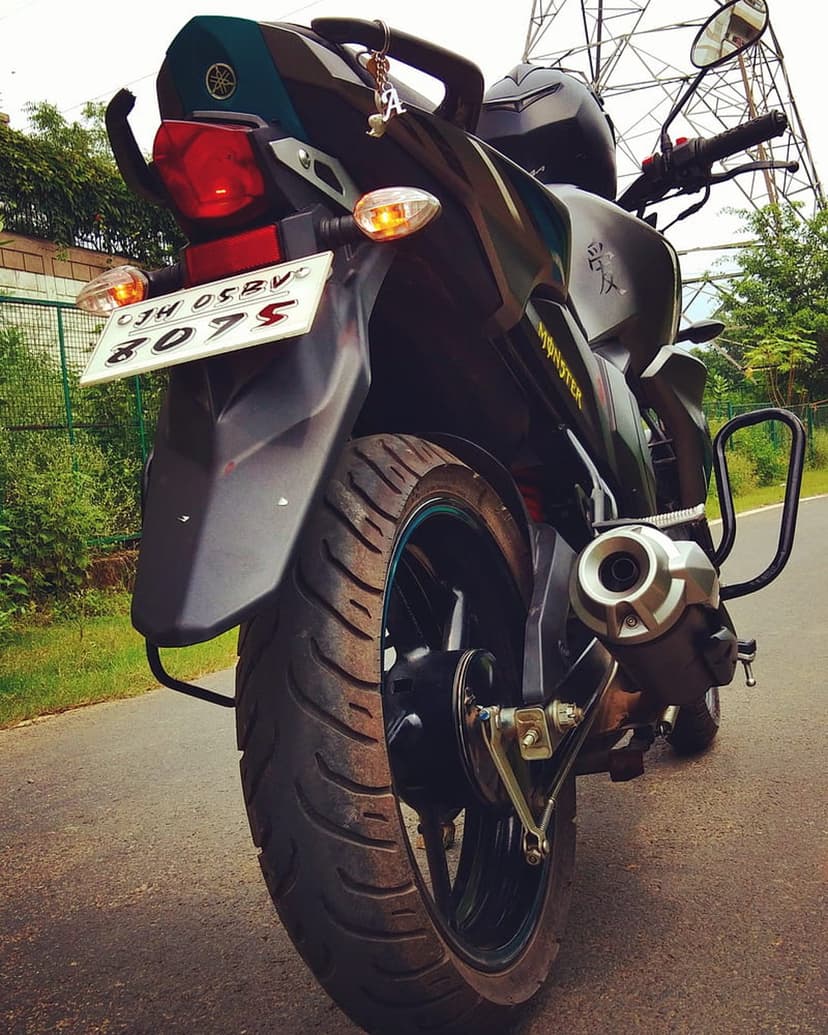 Yamaha motorcycle rear view showing a red taillight, license plate, metal exhaust, and thick tire tread.