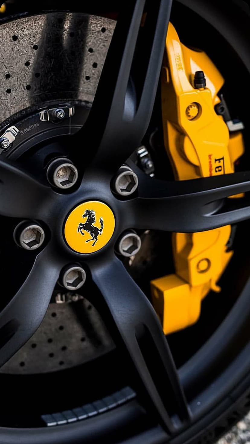 Black Ferrari multi-spoke wheel with a yellow Brembo brake caliper and perforated disc on a luxury sports car.