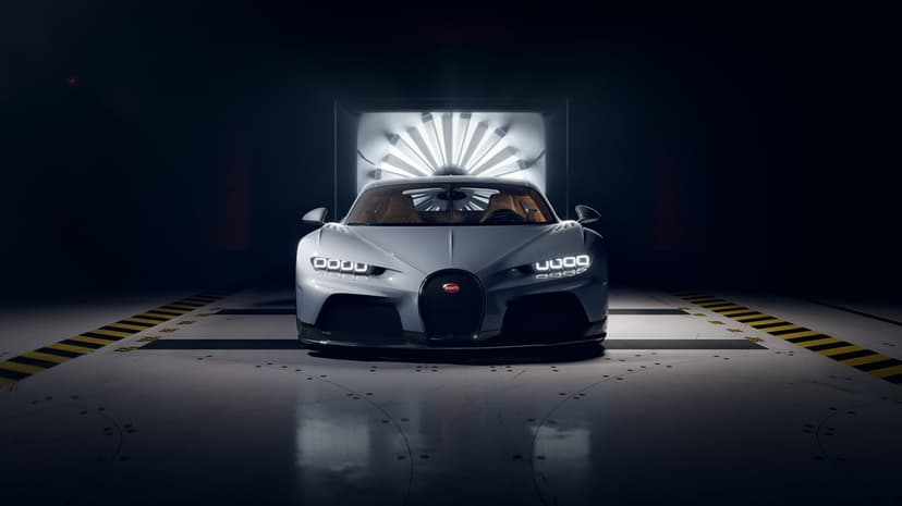 Silver Bugatti Chiron supercar with glowing LED headlights in a dark wind tunnel with a large backlit fan.