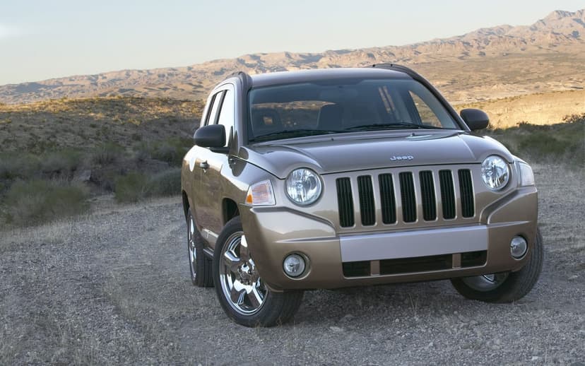Bronze Jeep Compass SUV parked on a gravel desert road with mountains under a clear sky in the background.