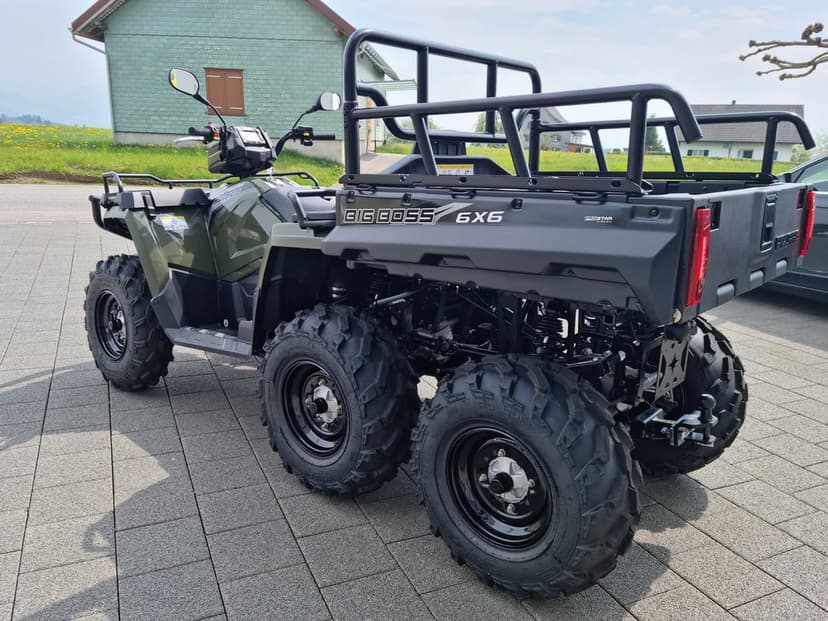 Green Polaris 6x6 Big Boss utility ATV with a black cargo rack parked on a grey paved driveway outdoors.