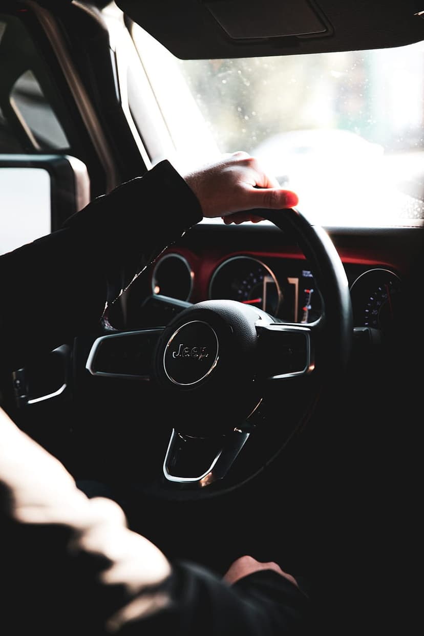 Hand on a Jeep steering wheel with bright sunlight hitting the dashboard instruments in a vertical composition.