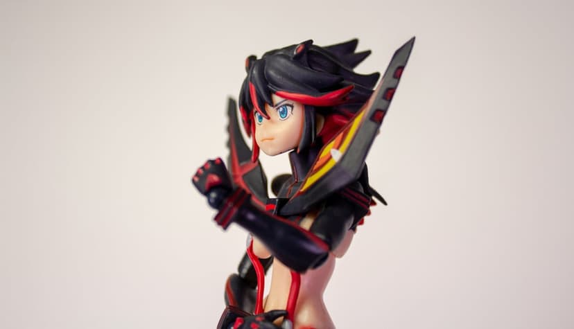 Ryuko Matoi action figure holding a red scissor blade, featuring spiky black hair and blue eyes in a portrait pose.