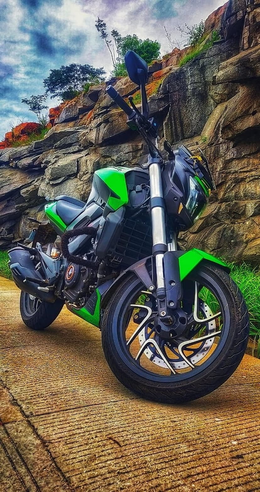 Neon green motorcycle on a stone path with rocky cliffs and a cloudy sky in a vertical mountain landscape.
