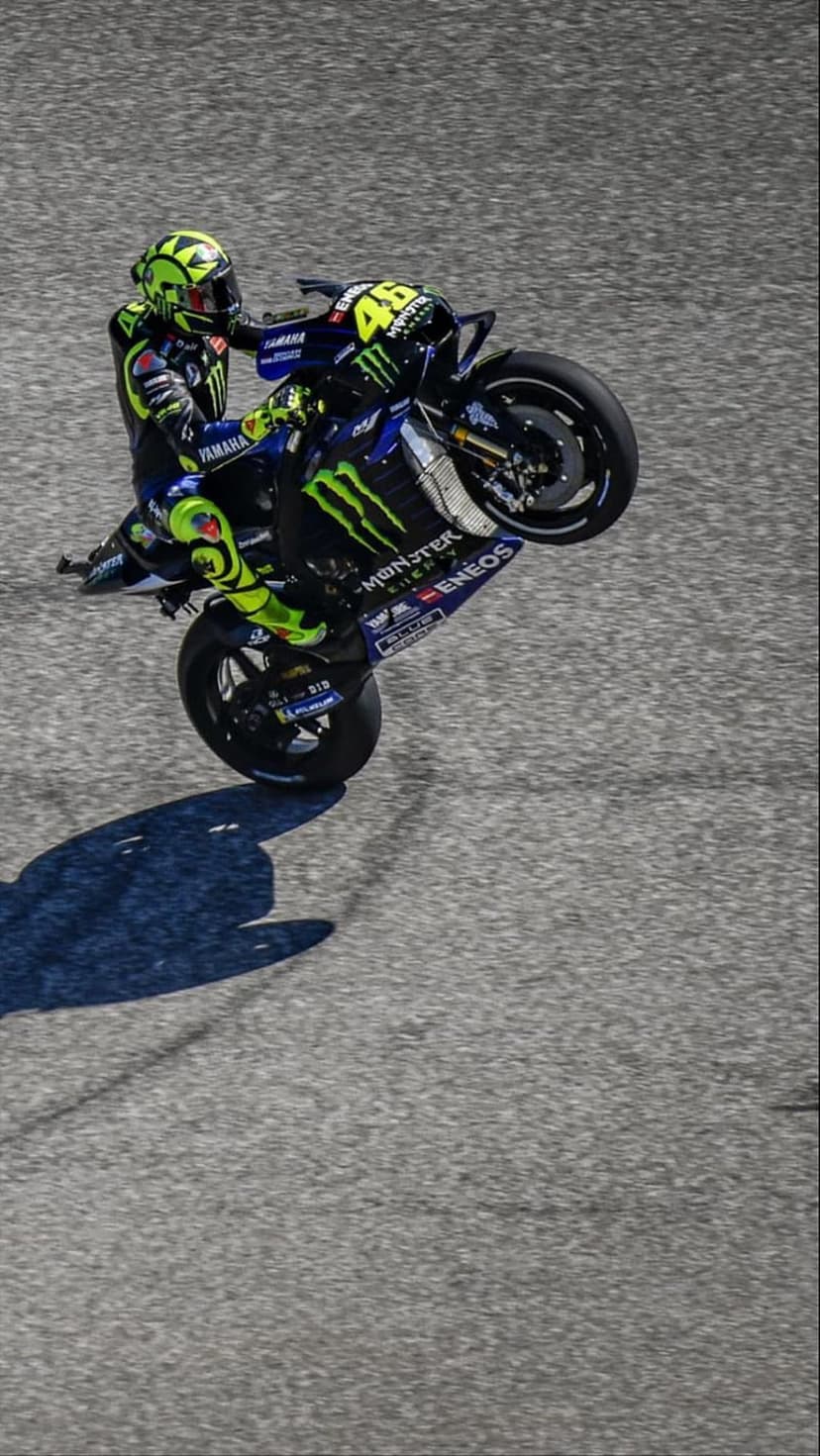 Valentino Rossi performs a wheelie on a Yamaha MotoGP bike while wearing a yellow and black racing suit.