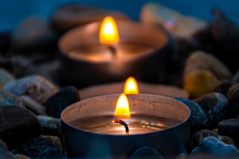 Two lit tea light candles glow amongst smooth dark river stones with a soft bokeh background for tranquility.