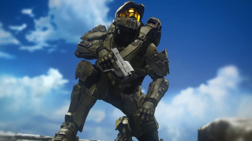 Master Chief in weathered olive green armor kneels with a pistol against a bright blue sky with white clouds.