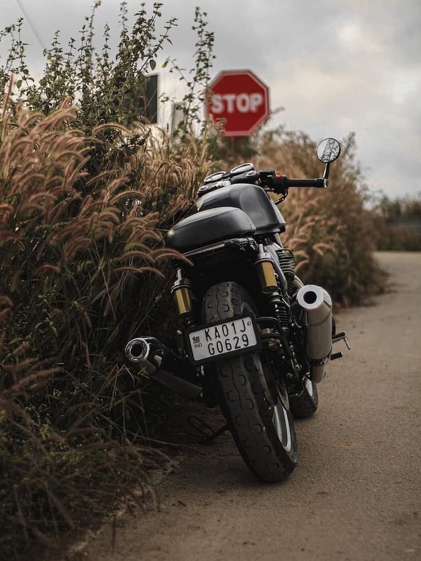 Classic black motorbike parked in tall dry grass beside a red octagonal stop sign on a rural dirt path.