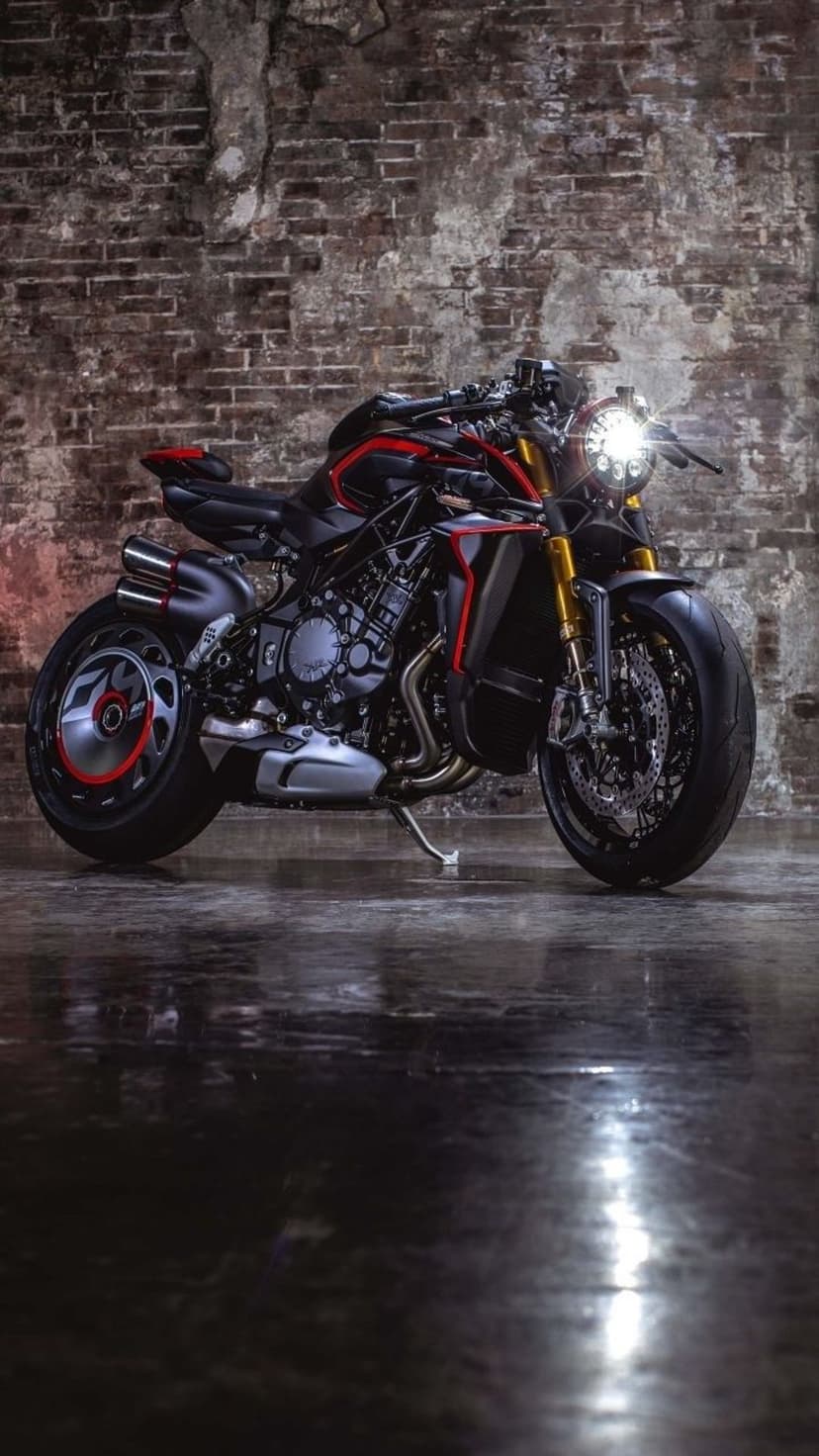 Black MV Agusta motorcycle with red frame accents parked before a brick wall on a wet, reflective floor surface.