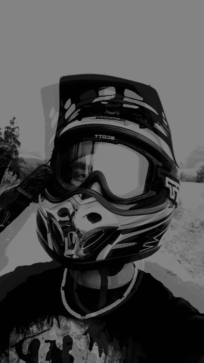 Motocross rider wearing a patterned helmet and Scott goggles with a reflected eye in a monochrome outdoor scene.