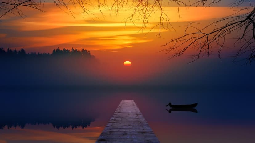 Weathered wooden dock points toward a silhouetted boat on a foggy lake under a fiery orange sunset sky.