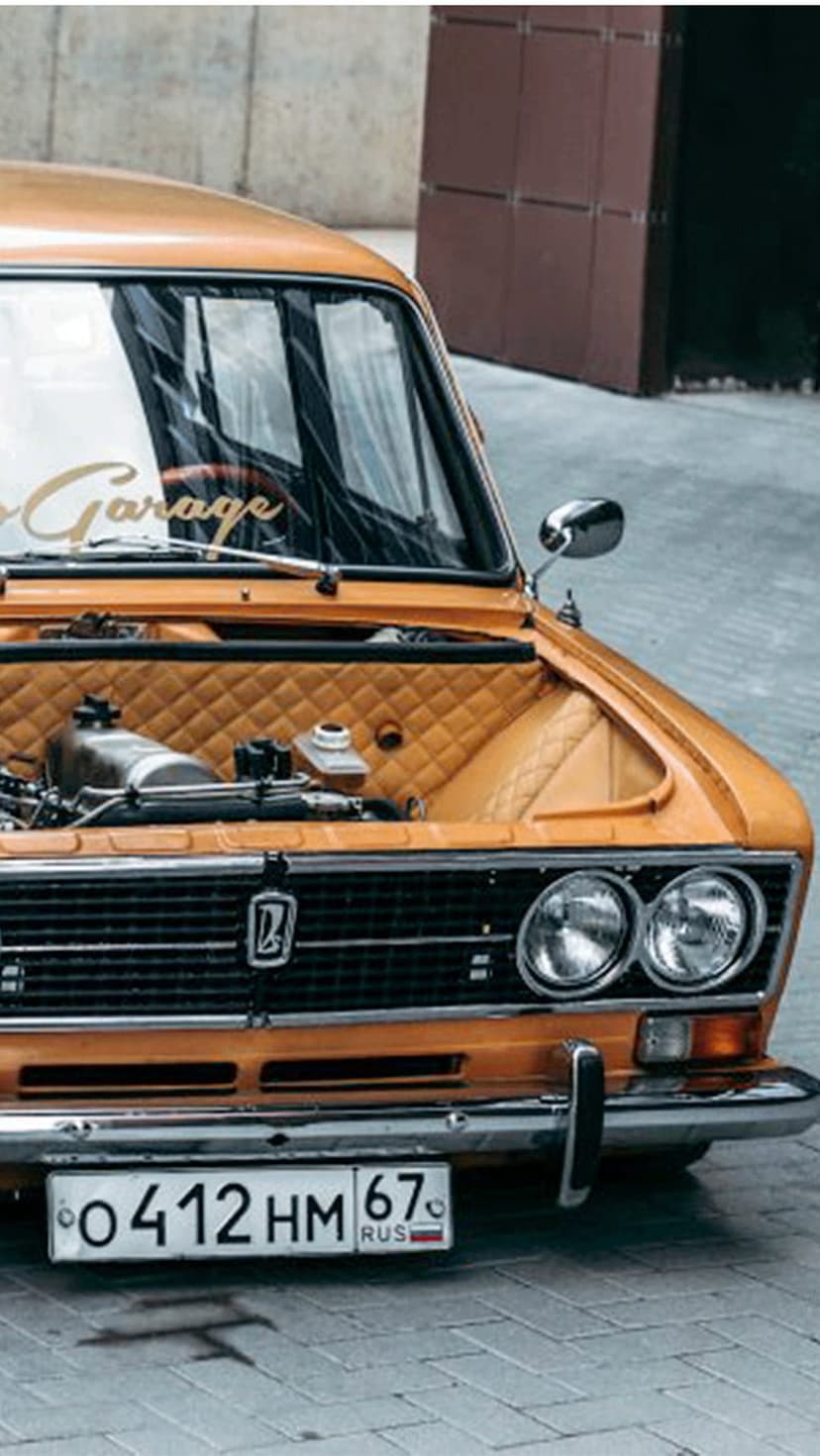 Classic orange VAZ car showcases a custom quilted engine bay, chrome grille, and circular headlights in close-up.