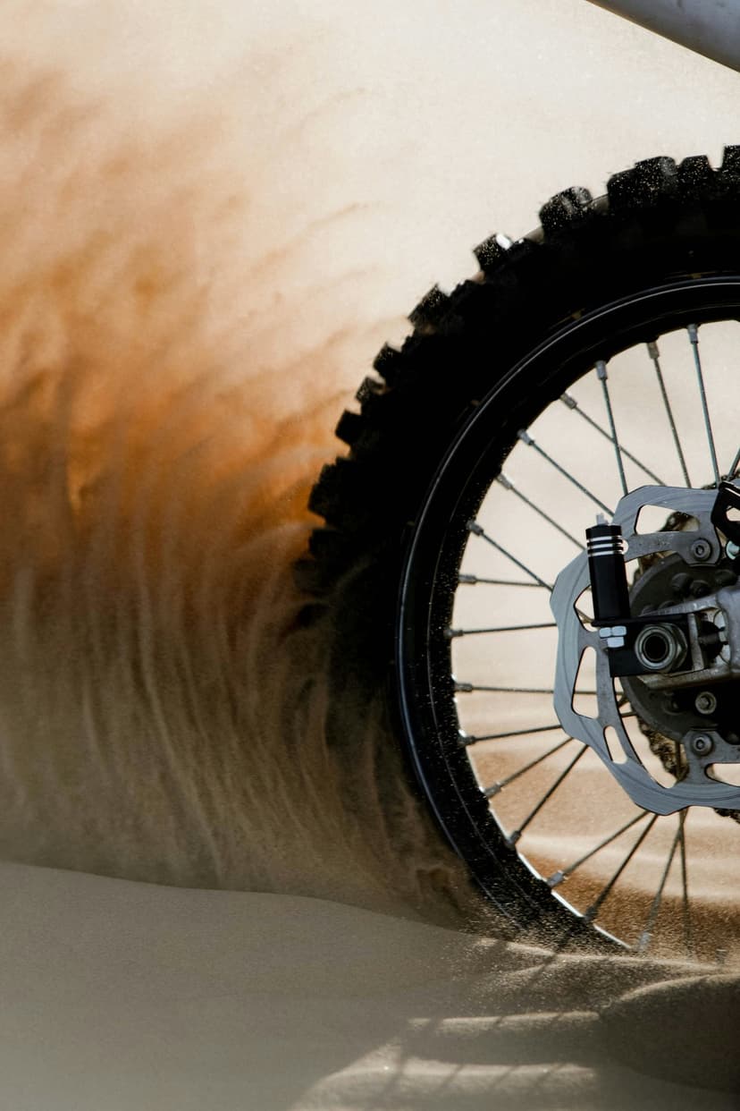 Knobby dirt bike tire spinning through a golden sand dune, throwing a dense cloud of fine dust into the air.