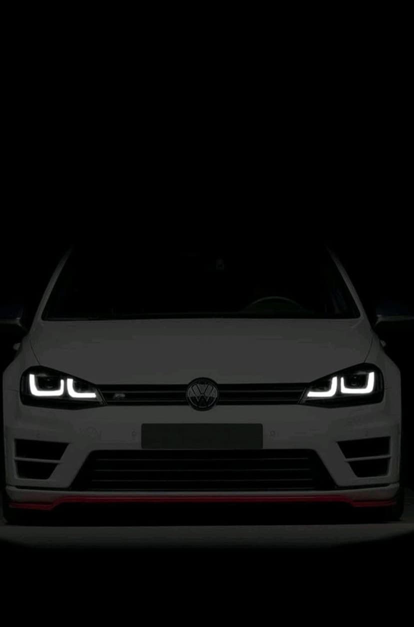 White Volkswagen Golf R with illuminated LED headlights and a central badge against a dark background.