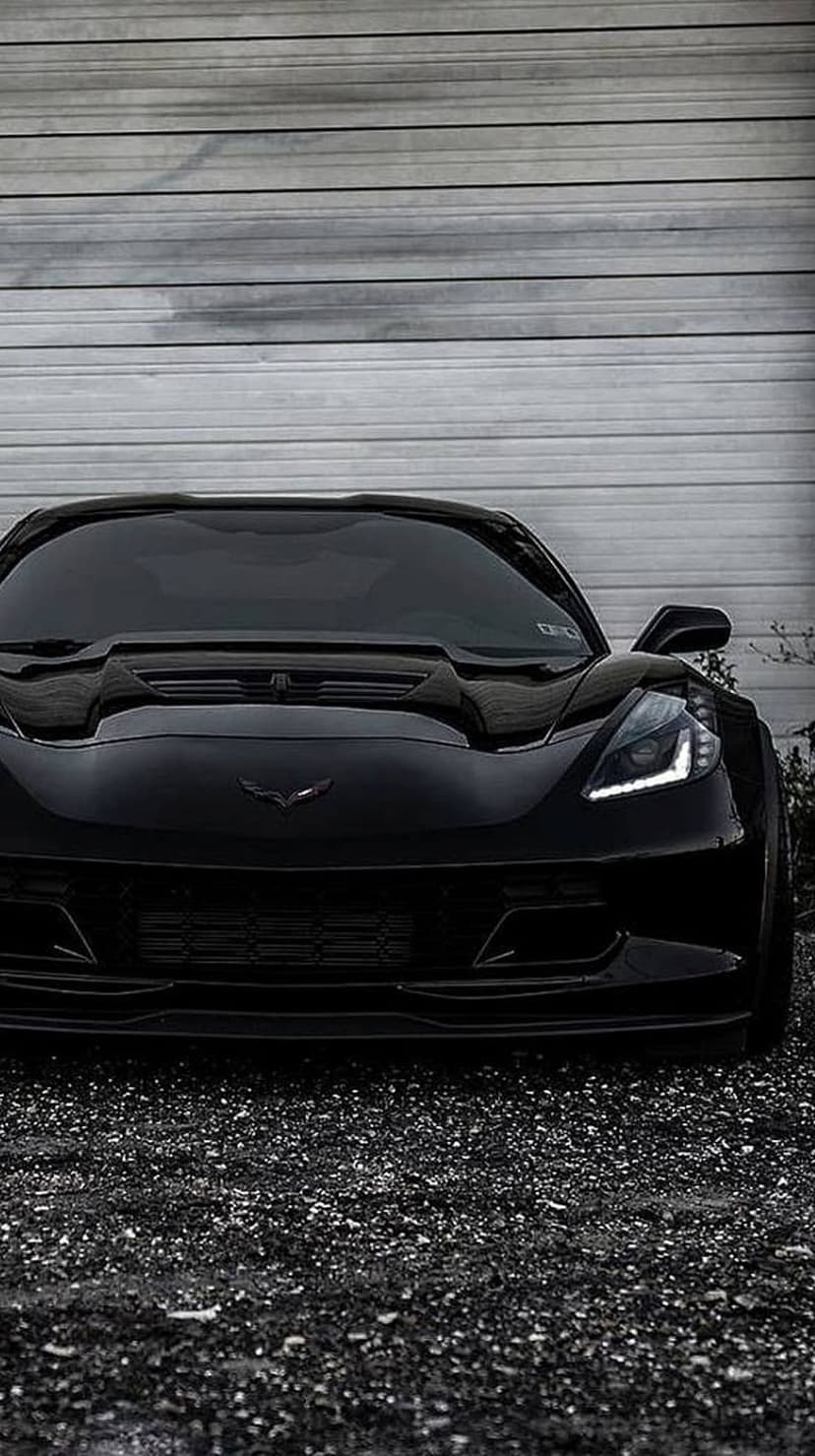 Black Chevrolet Corvette Z06 parked at a low angle in front of a gray metal garage door on dark asphalt.