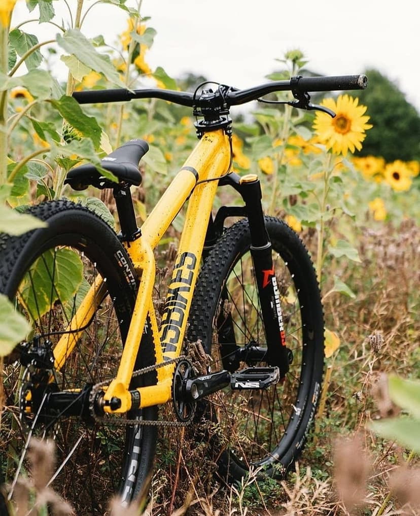 Yellow dirt jump bike with knobby tires stands in a field of sunflowers with lush green leaves and golden petals.