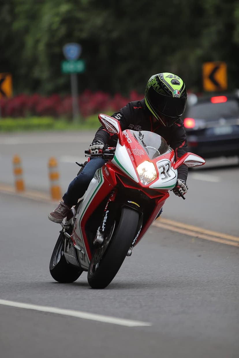 Motorcyclist in a black and yellow helmet leans a red sportbike numbered 32 into a turn on a paved road.