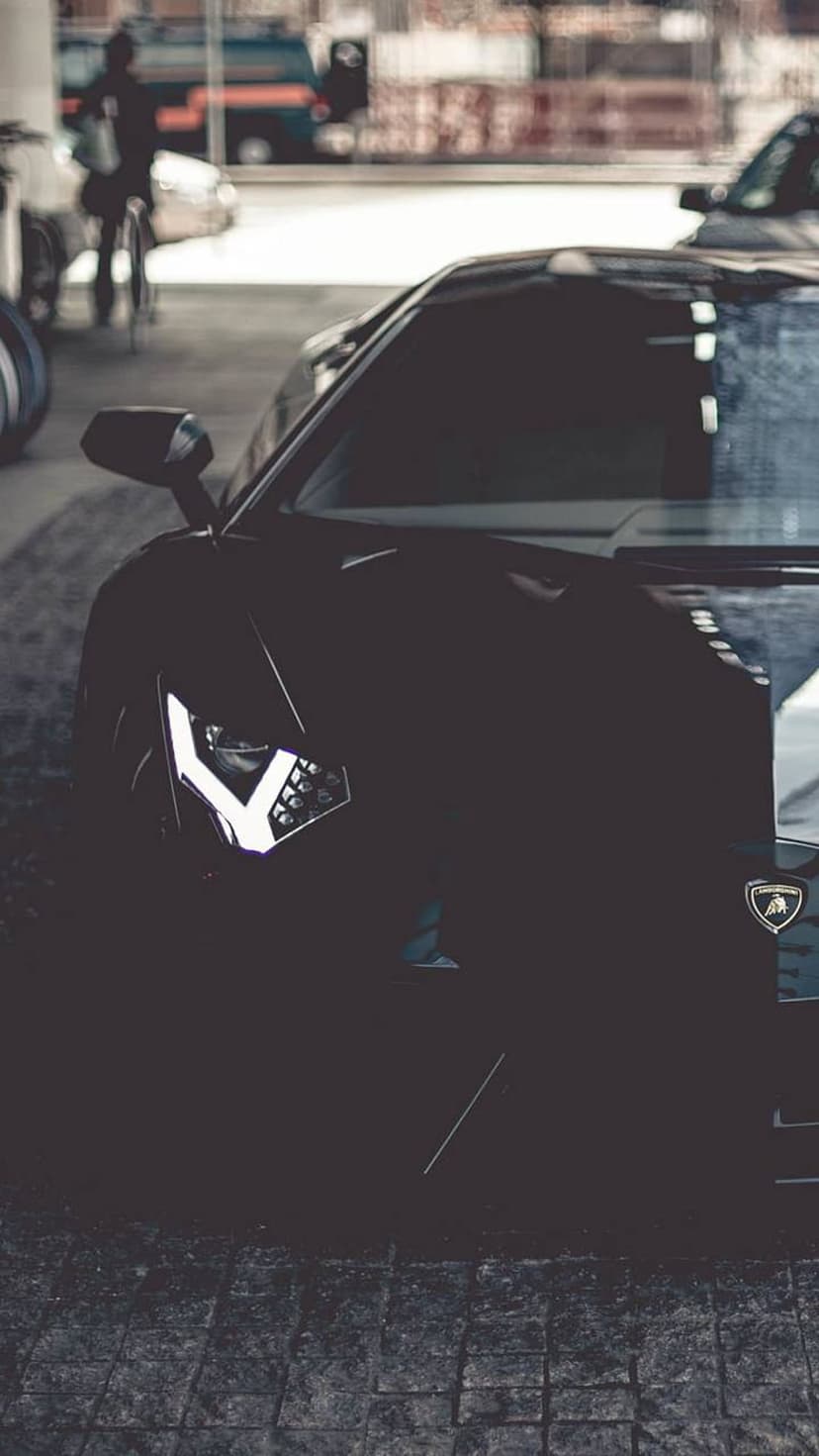 Lamborghini Aventador headlight showing sharp LED patterns on a black metallic bumper with low angle lighting.