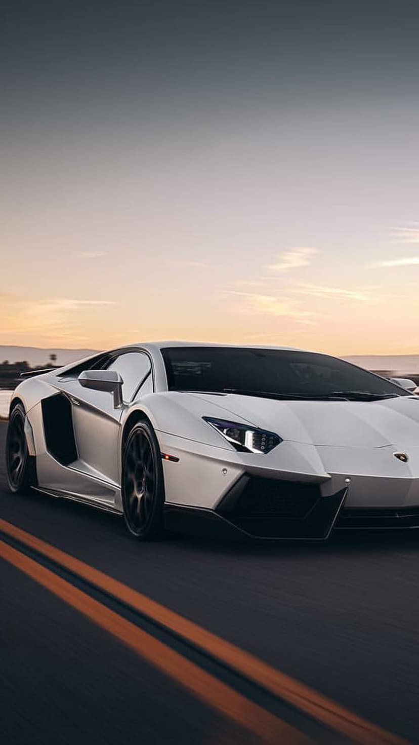 White Lamborghini Aventador speeds on a highway with orange lane markers under a glowing golden sunset sky.