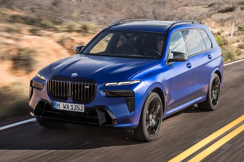 Blue BMW X7 SUV driving on a desert highway with motion blur, black wheels, and aggressive matte front grille.