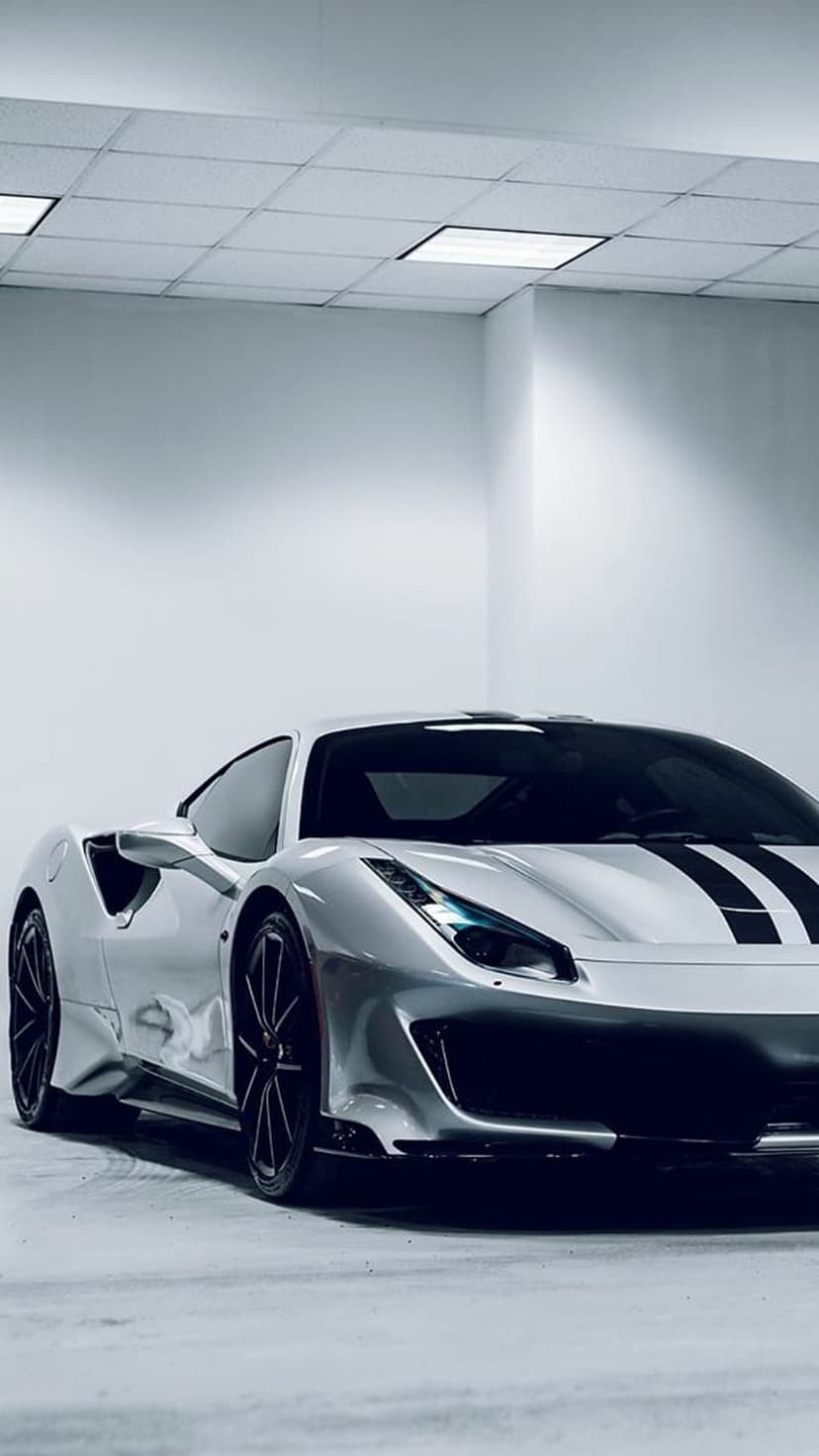 Silver Ferrari 488 Pista with black racing stripes and dark rims parked in a well-lit indoor studio space.