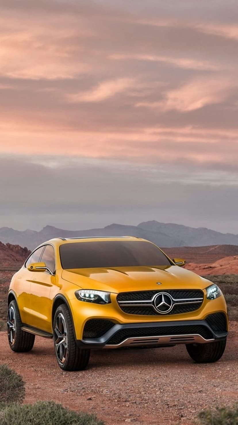Yellow Mercedes SUV concept car parked on a sandy desert road with jagged mountains under a soft twilight sky.
