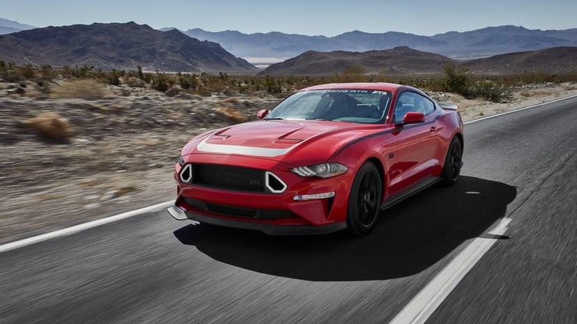 Red Ford Mustang RTR driving fast on a desert road with mountains in the distance and motion blur on the asphalt.