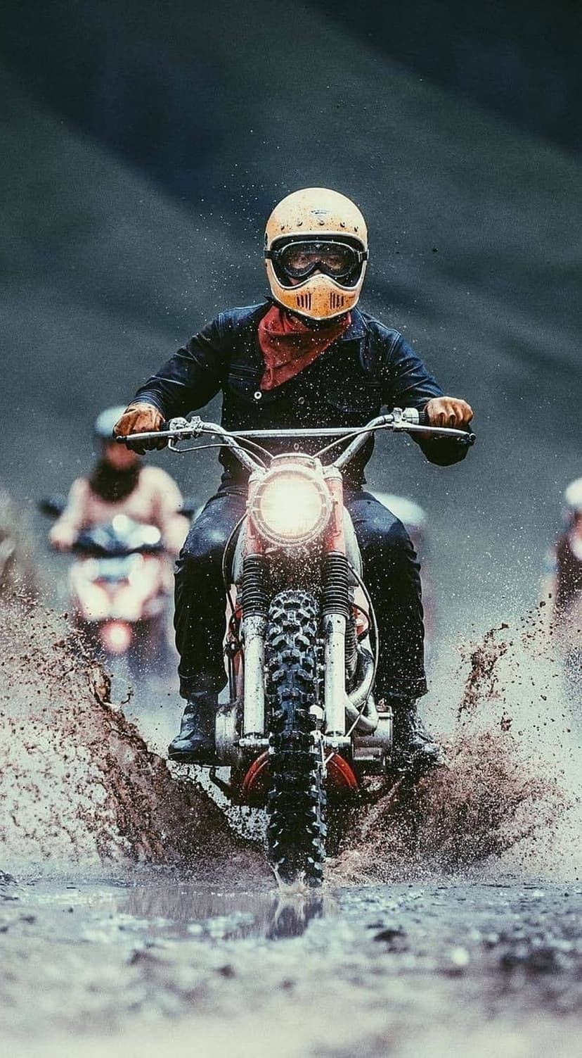 Motorcyclist in a yellow helmet and vintage gear splashes through a muddy puddle, throwing up dark water and silt.