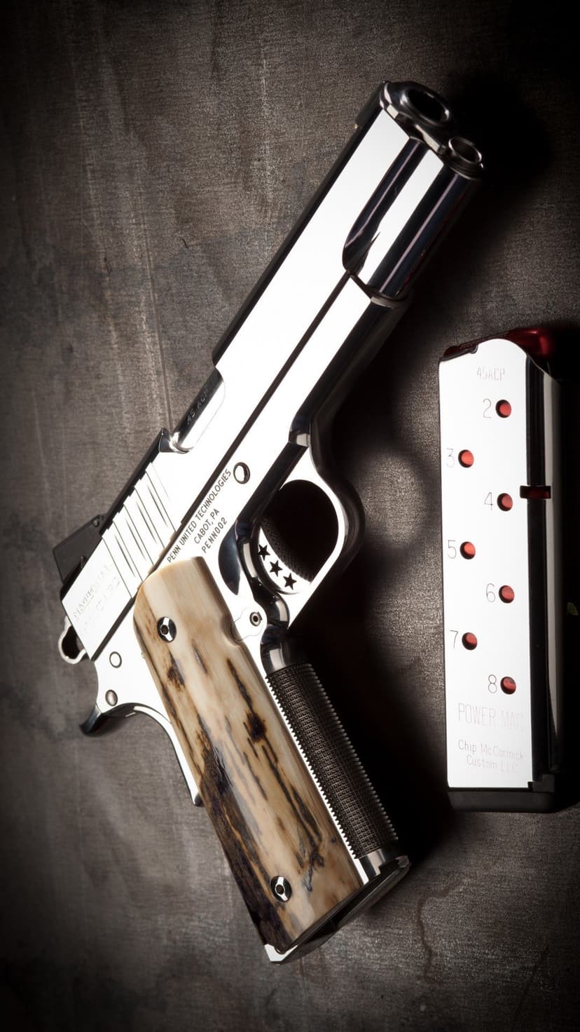 1911 pistol with stag horn grips and engraved stars lies near a loaded magazine on a dark textured surface.