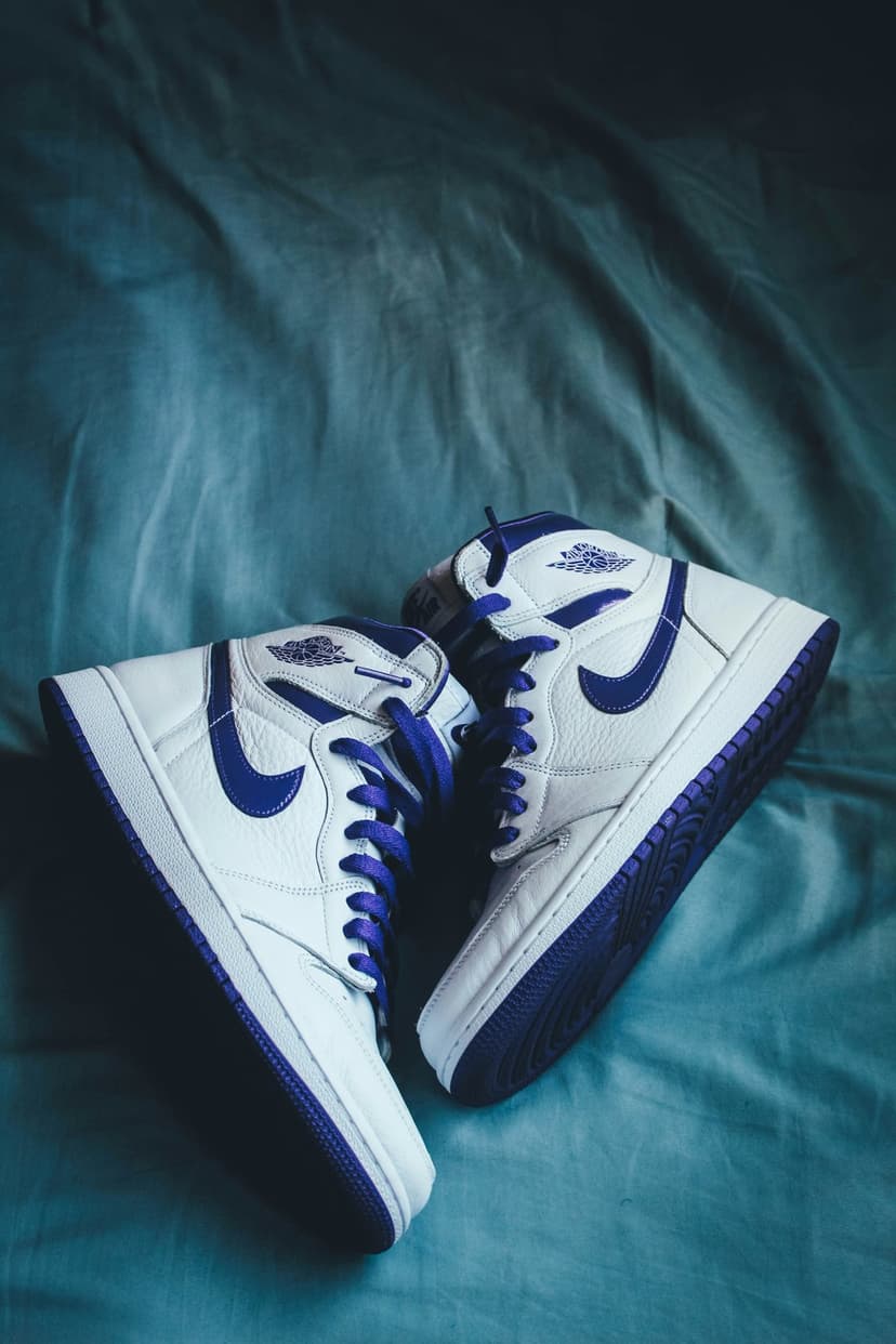 Air Jordan 1 sneakers in blue and white leather sit atop a textured teal cloth surface with loose and tied laces.