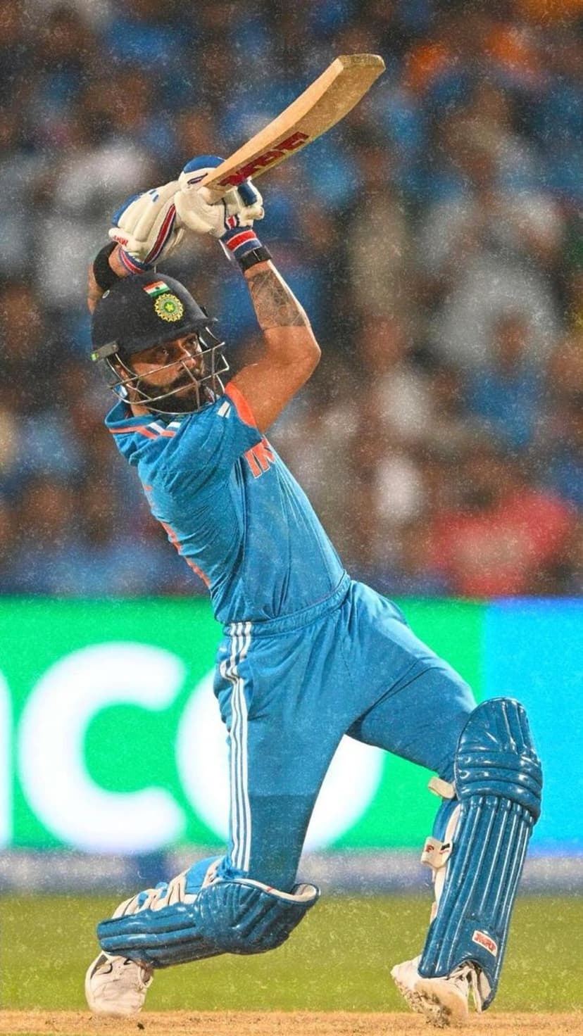 Virat Kohli bats in a blue Indian cricket jersey and helmet during a night match with blurred stadium lights.