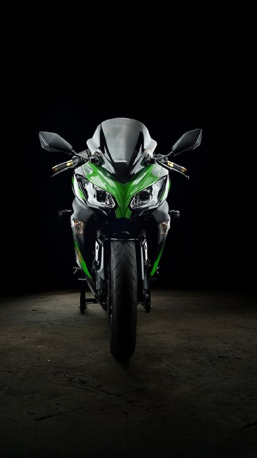 Kawasaki Ninja sportbike with green fairings and lit headlights stands on a dark floor against a black backdrop.