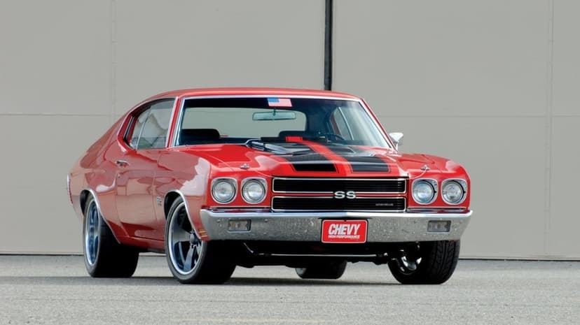 Red 1970 Chevrolet Chevelle SS with black racing stripes and chrome bumpers parked on asphalt against a tan wall.