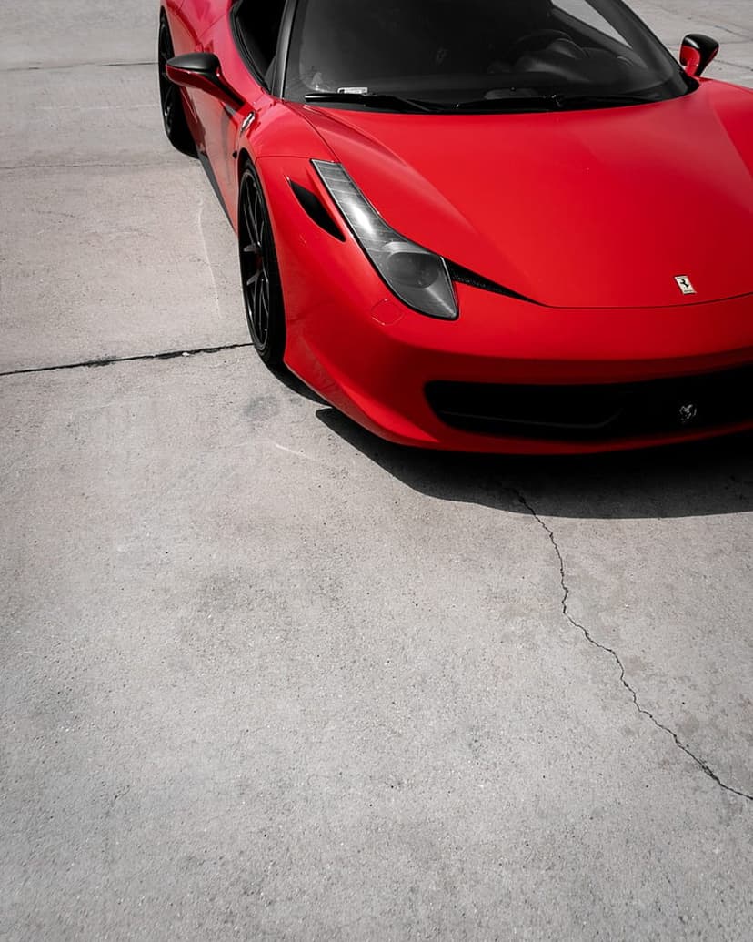 Ferrari sports car with a red fender and black rim sits on a cracked concrete surface under dramatic lighting.