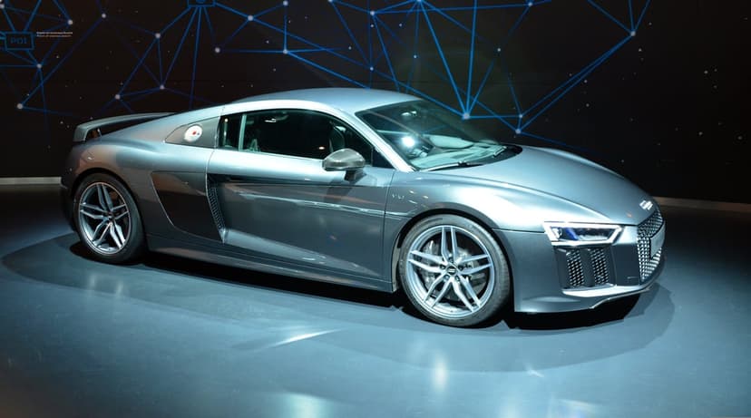 Silver Audi R8 sports car parked on a reflective blue floor featuring futuristic light patterns and dark shadows.