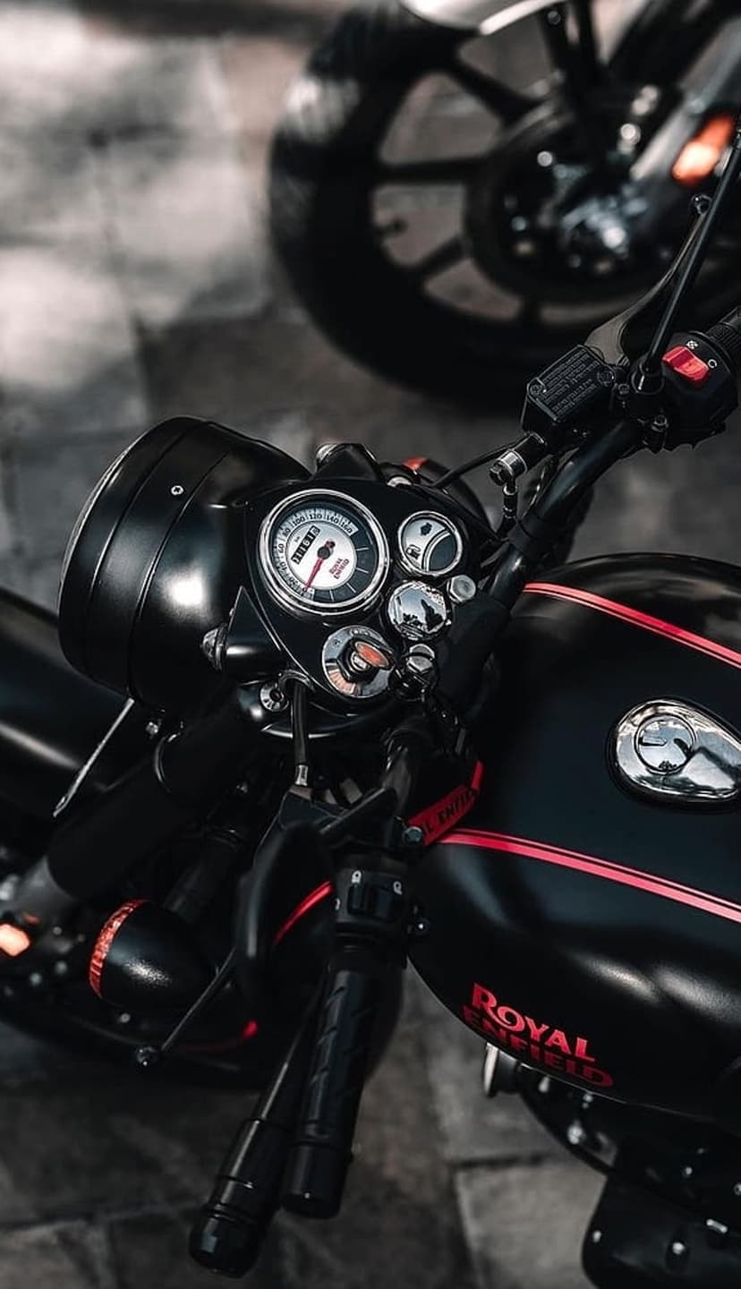 Royal Enfield motorcycle dashboard with a chrome circular speedometer, red pinstripes, and a matte black fuel tank.