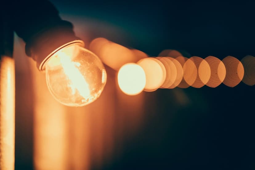 Incandescent light bulb with a visible glowing filament in focus against a backdrop of blurred golden bokeh orbs.