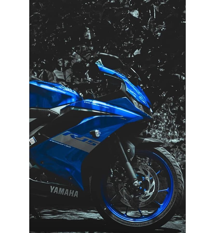Yamaha R15 motorcycle in electric blue showcases front fairing and brake disc against a dark foliage background.