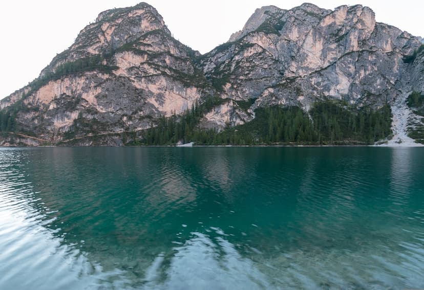 Jagged Dolomite mountains reflect in a turquoise lake with a small white boat near a green pine forest shore.