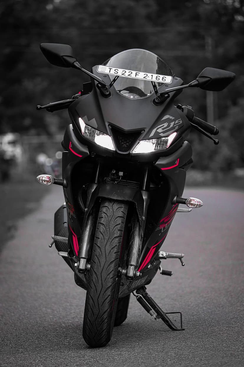 Yamaha R15 sportbike in matte black with red accents and illuminated headlights against a soft blurred background.