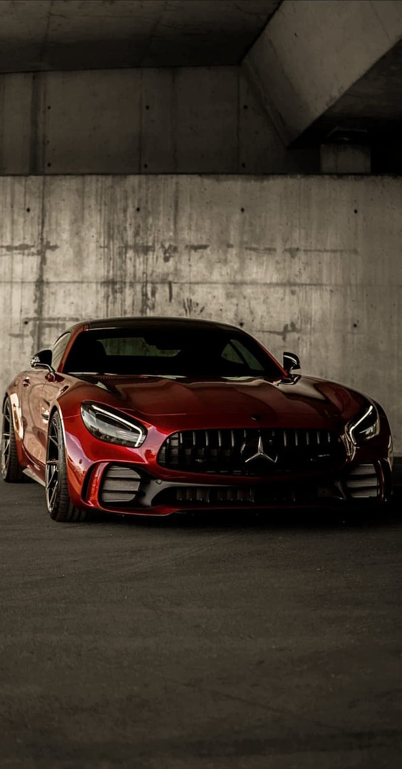 Scarlet Mercedes-AMG GT parked on dark asphalt inside a textured concrete parking garage with moody shadows.