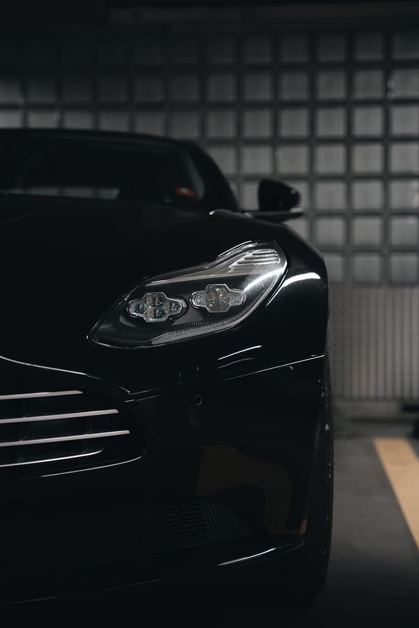 Luxury car headlight with sharp LED accents reflecting a glass block wall inside a dark industrial garage setting.