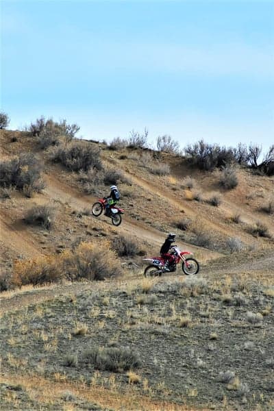 Two motorcyclists riding dirt bikes on a dry, hilly terrain