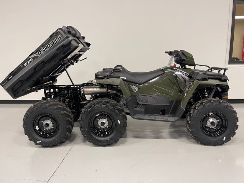 Olive green six-wheeled Polaris Sportsman ATV with an elevated rear dump bed in a bright white showroom.