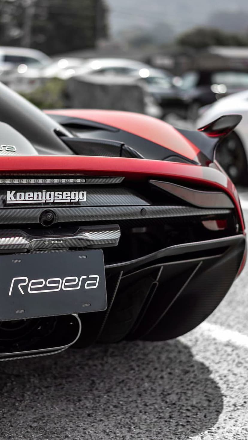 Red Koenigsegg Regera rear showing carbon fiber diffuser, active wing, and brand badge on a sunny asphalt road.